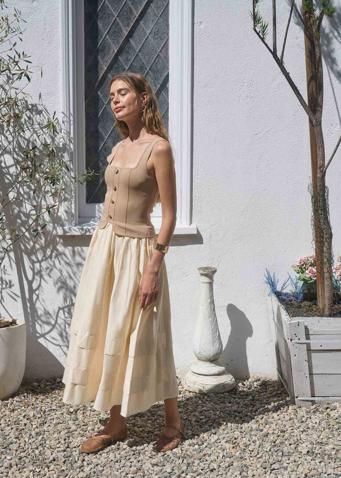Khaki midi dress with button-front bodice and pleated skirt on model in outdoor courtyard setting.