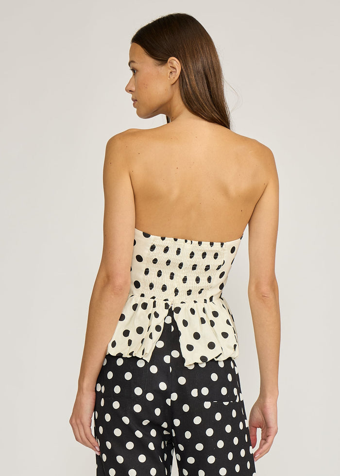 Strapless peplum top with cream polka dot bodice and black polka dot skirt, shown from back.