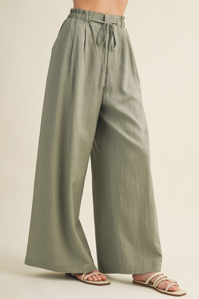 Sage green wide-leg pants with drawstring waist and pleated front, worn with tan slide sandals.