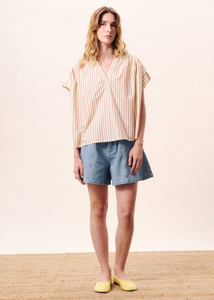 Woman wearing cream and tan striped short-sleeve wrap top with blue denim shorts and yellow shoes.
