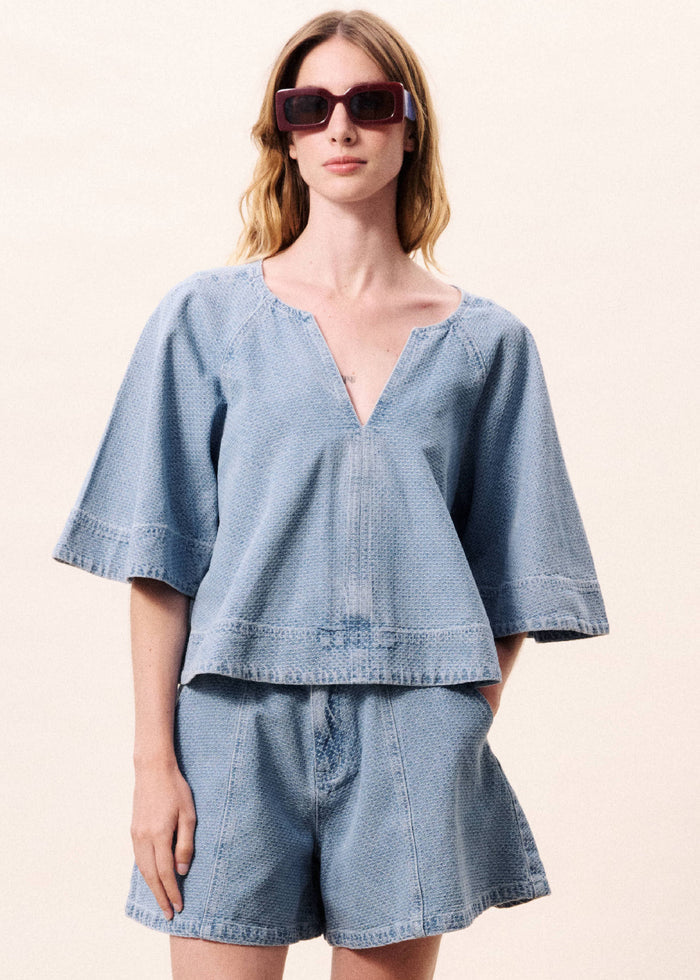 Light blue denim v-neck top with short flared sleeves and horizontal seaming detail at waist.