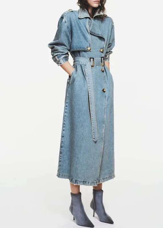 Light blue denim trench coat with collar, chest pocket, belt, and button front closure worn with gray ankle boots.