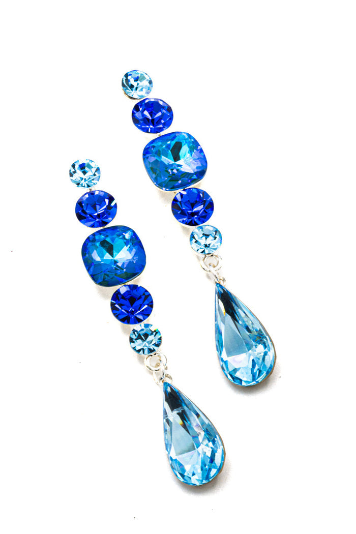 A pair of drop earrings featuring faceted blue and light blue rhinestones in a silver-tone setting, arranged on a plain white background.