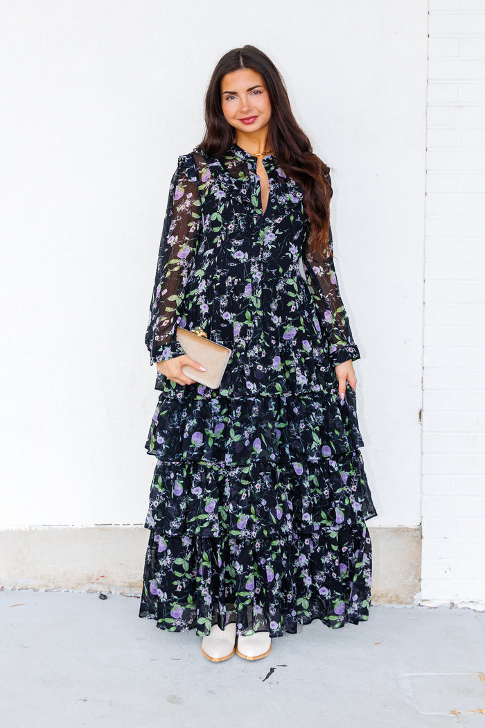 Black maxi dress with purple and green floral print, long sleeves, and tiered skirt design.