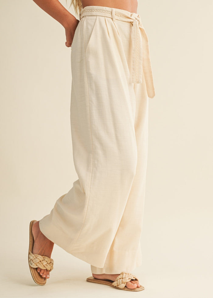 Cream pleated palazzo pants with wide legs and a braided tie belt worn at the waist.