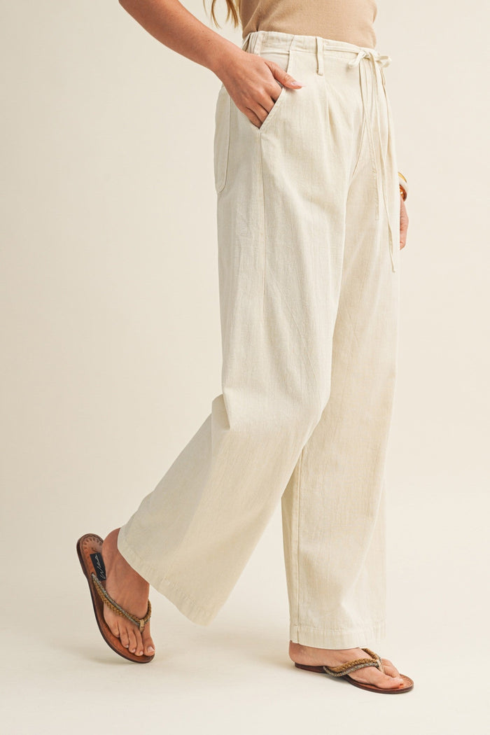 Cream straight-leg pants with drawstring waist and side pockets, shown on model wearing brown sandals.