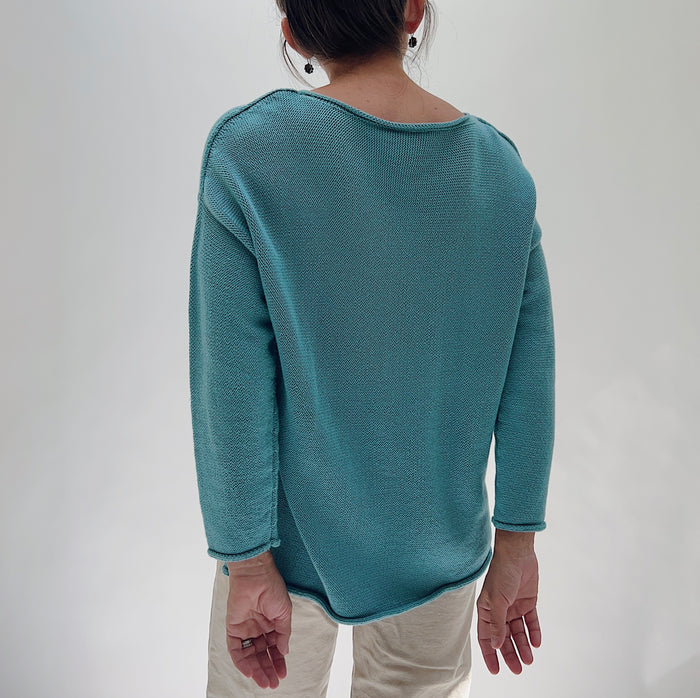 Shannon Passero Handloomed Cotton Emerson Pullover in Tide Blue — rear view showing the smooth open-stitch knit back, wide boat neckline, dropped shoulders, and curved hem, worn with cream trousers on a white background