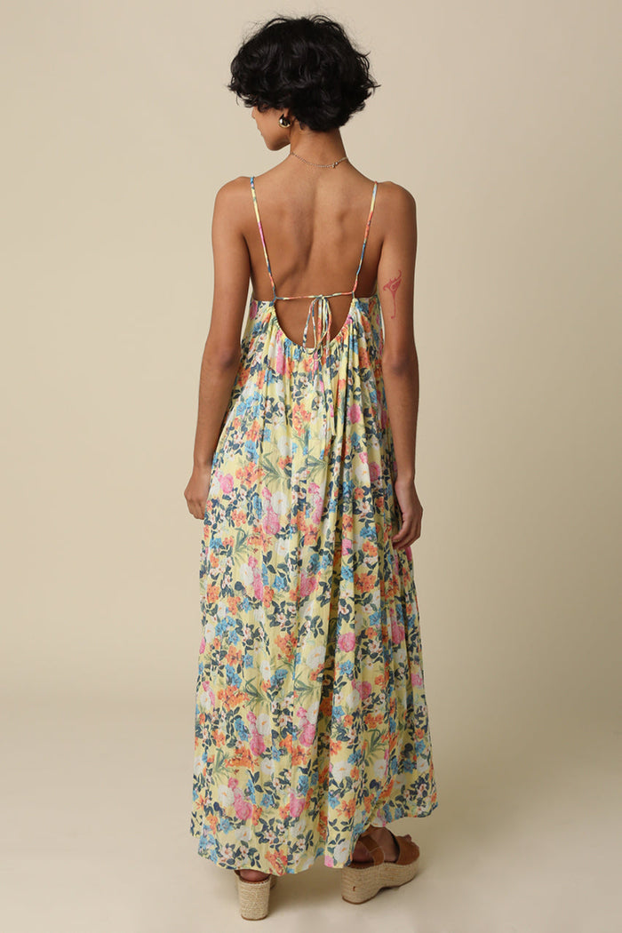 Woman wearing sleeveless maxi dress with colorful floral print and open back tie detail.