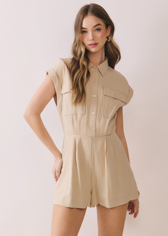 Beige short-sleeved collared romper with button front, chest pockets, and pleated skirt worn by model.