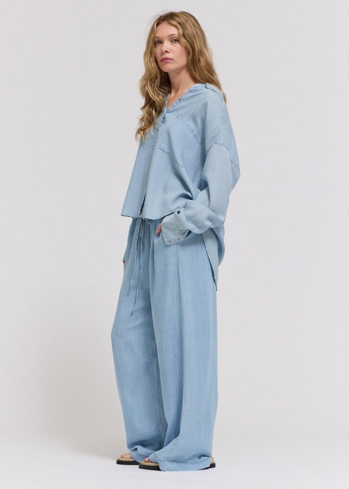 Woman wearing light blue chambray straight-leg pants with matching button-up shirt and drawstring waist.
