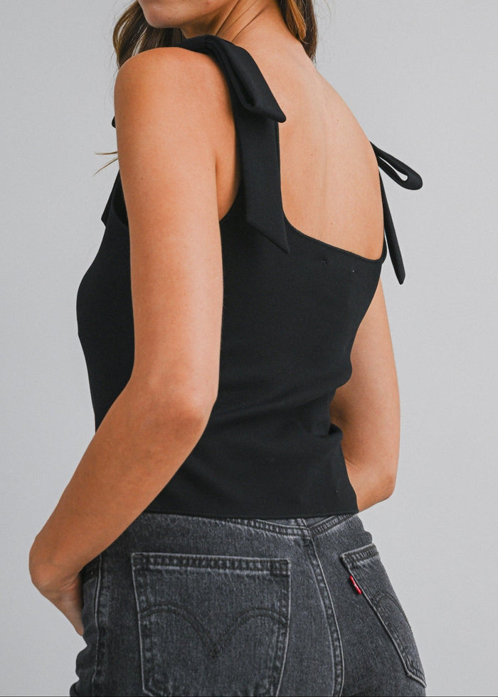 Black sleeveless crop top with open back and tie shoulder straps, worn with dark denim jeans.