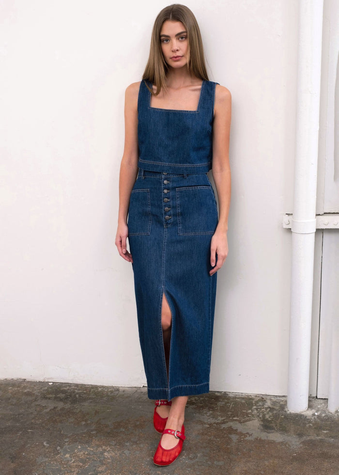 Dark blue denim midi skirt with button front and front slit, styled with matching denim tank top.