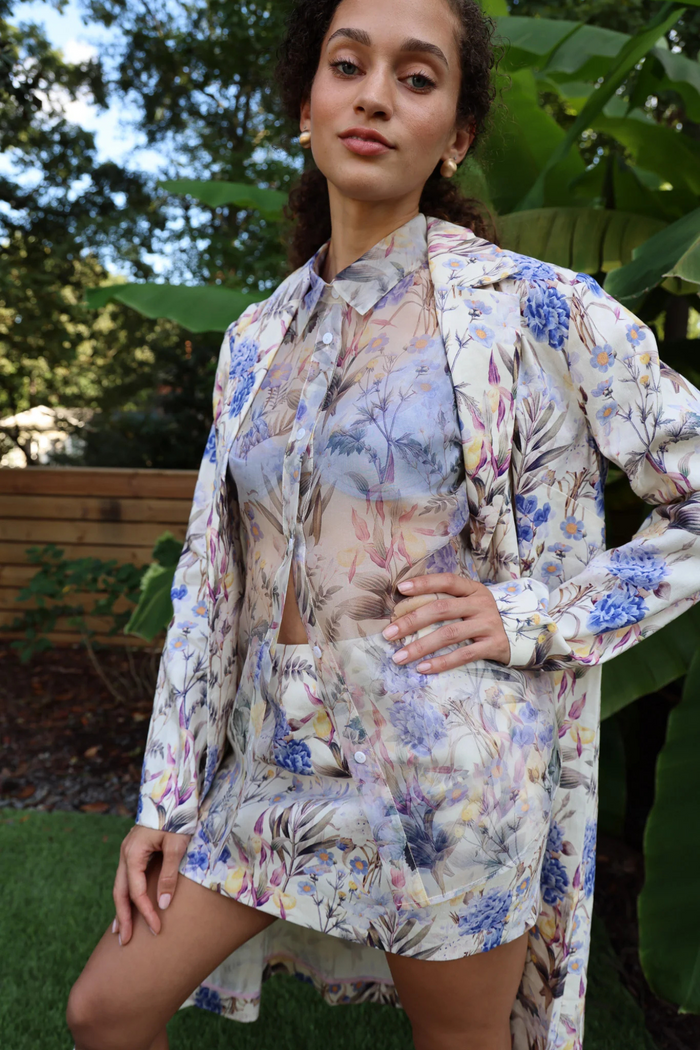 Woman wearing a cream button-down shirt with blue, purple, and pink floral print, styled outdoors.