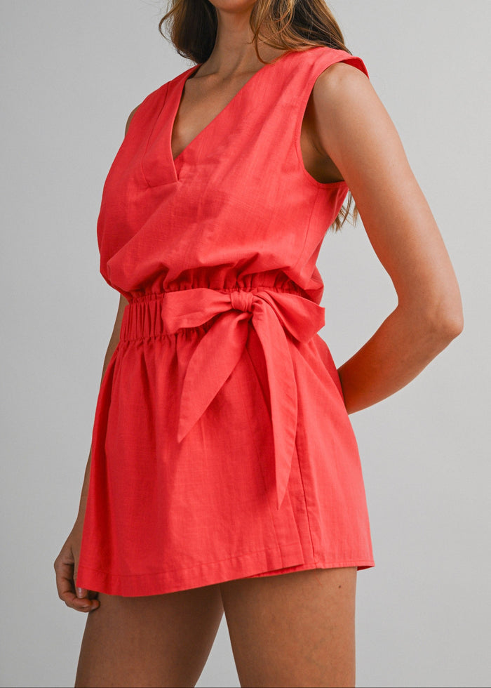 Red sleeveless V-neck romper with tied waist detail and gathered skirt on model.