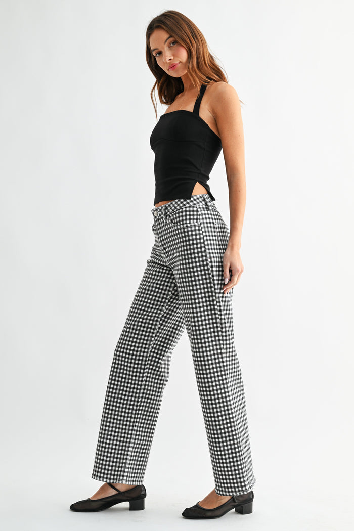Woman wearing black and white gingham mid-rise jeans with a black halter top and black heeled shoes.