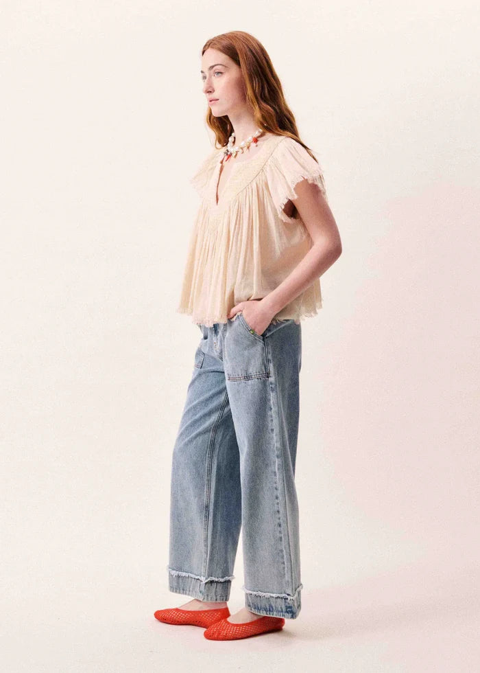 Woman wearing a cream pleated short-sleeve top with a tie neckline, paired with light blue jeans and red socks.