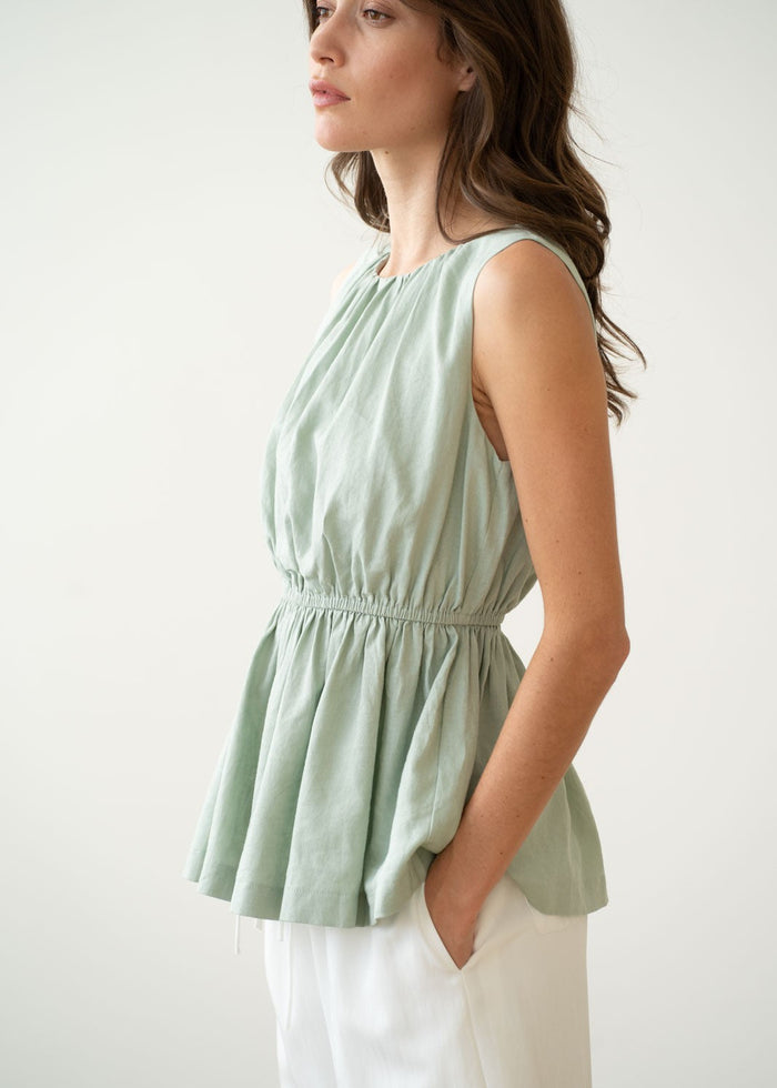 Sage green sleeveless peplum tank top with cinched waist, worn with cream pants.