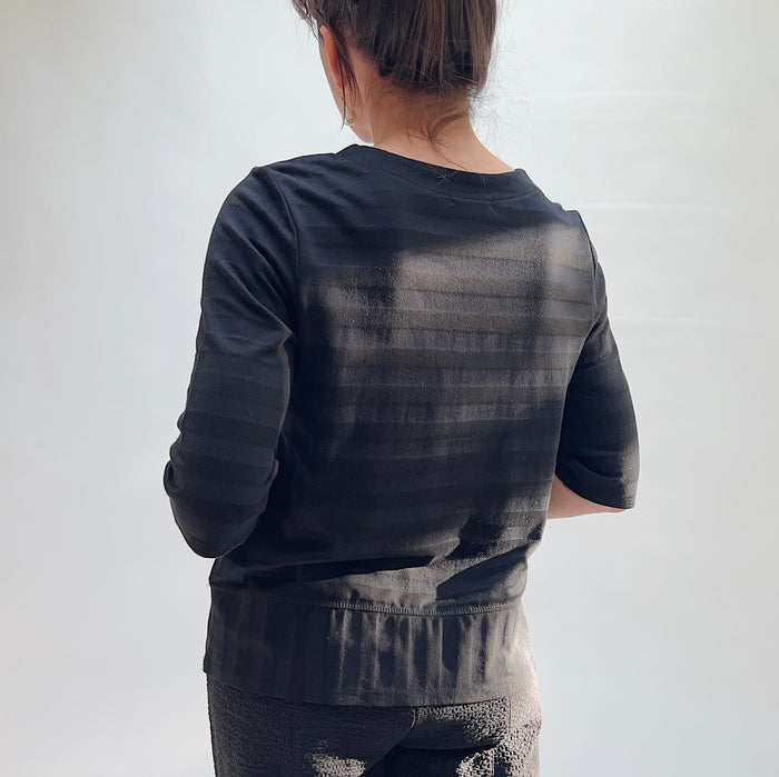 Back view of model wearing Habitat black shadow stripe elbow sleeve top, showing tonal stripe texture, elbow sleeves, and layered curved hem