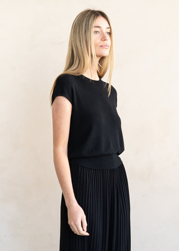 Woman wearing black short-sleeve knit top with crew neckline, shown from the side.
