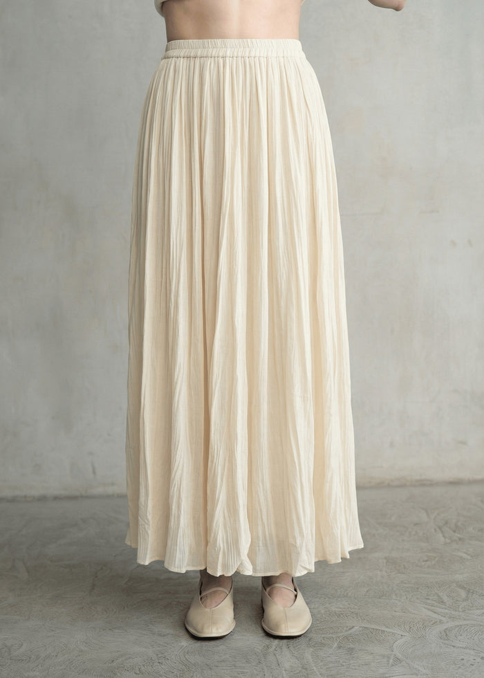 Cream crinkled maxi skirt with pleated detail and elastic waistband on model wearing neutral flats.