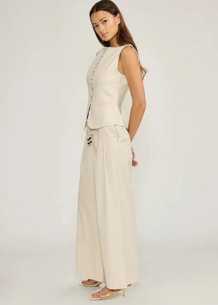Woman wearing cream sleeveless button-front vest and cream wide-leg pants with side pockets.