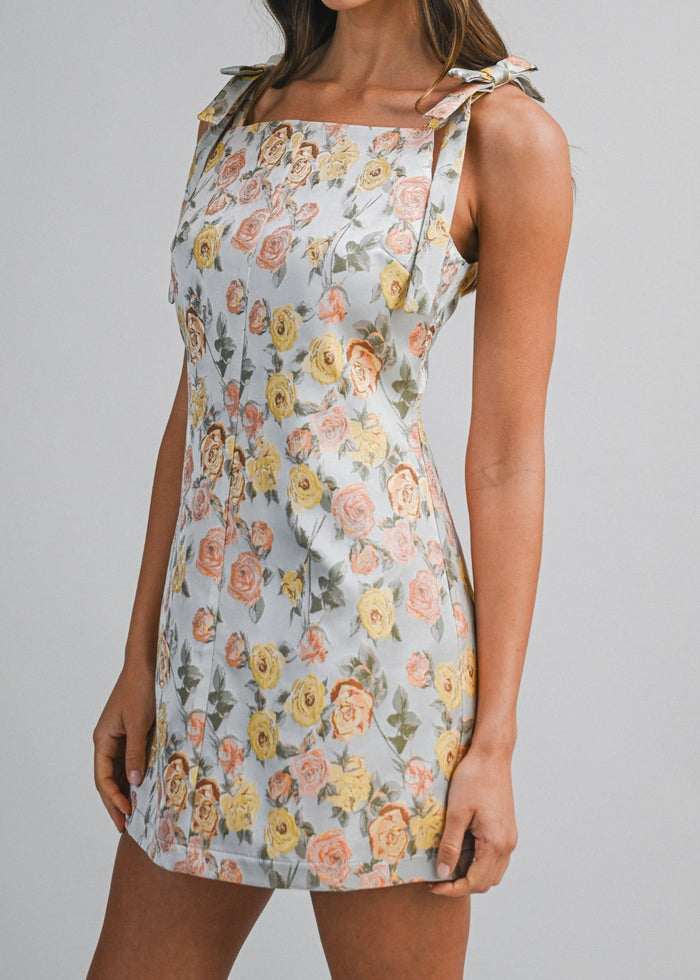Sleeveless mini dress with multicolored floral jacquard print and tie shoulder straps on white background.