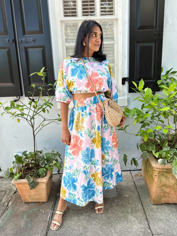 Woman wearing a white cropped top with multicolored floral print in blue, yellow, and pink tones.
