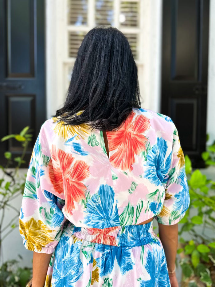 Pink top with red, blue, yellow and green floral print, three-quarter sleeves, and notch neckline.