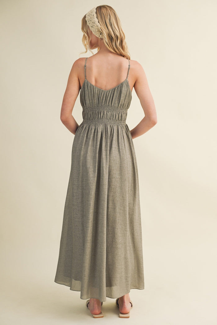 Woman wearing sage green sleeveless maxi dress with ruched bodice and thin straps, shown from back.