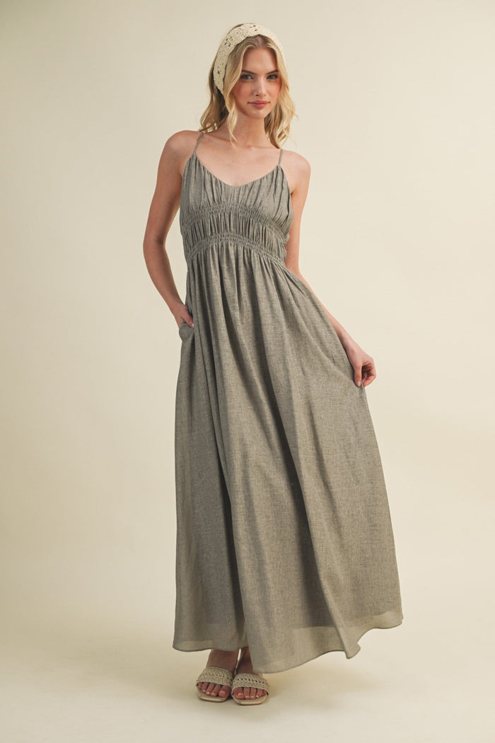 Sage green sleeveless maxi dress with gathered bodice and side pockets, worn with beaded sandals.