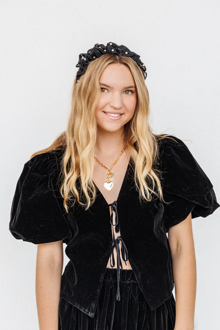Black velvet puff sleeve top with front tie closure, worn with a black scrunchie headband.