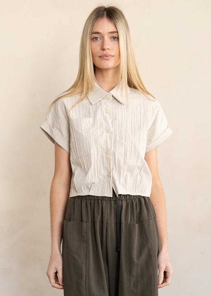 Beige pinstriped short-sleeve button-down shirt with collar on model wearing olive pants.