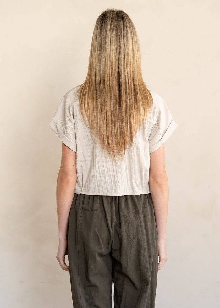 Woman wearing white button-down shirt with short sleeves and olive green pants, shown from behind.