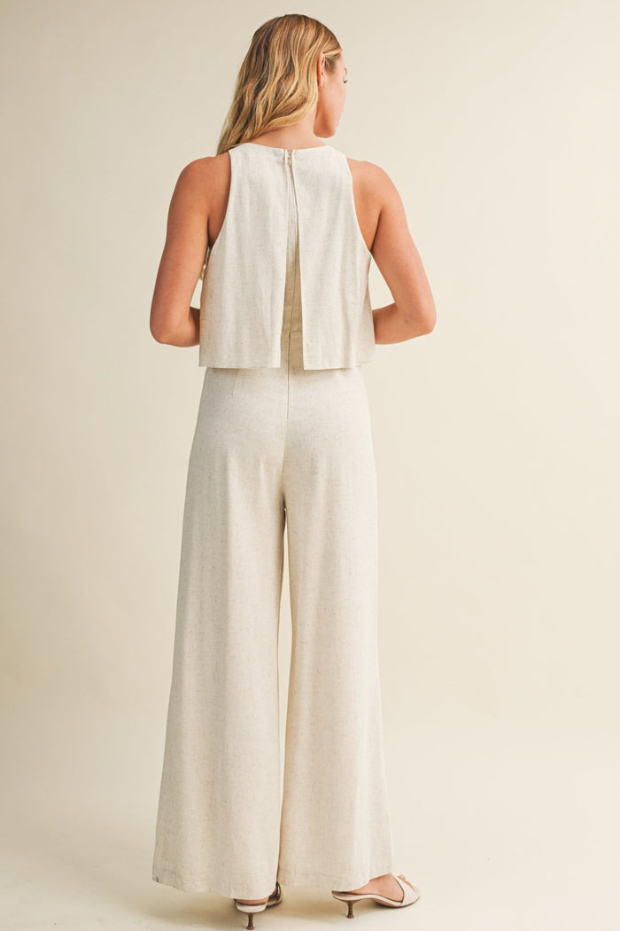Woman wearing cream linen sleeveless jumpsuit with wide legs and open back detail, shown from behind.