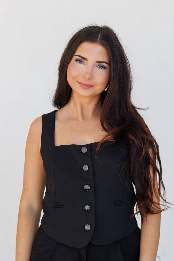 Black sleeveless suit vest with square neckline and five metallic buttons down the front.