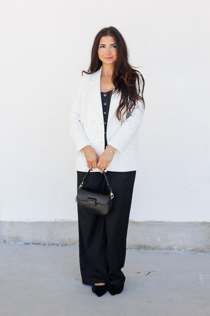 White blazer with notch lapels and dark buttons worn over a black top with black trousers.