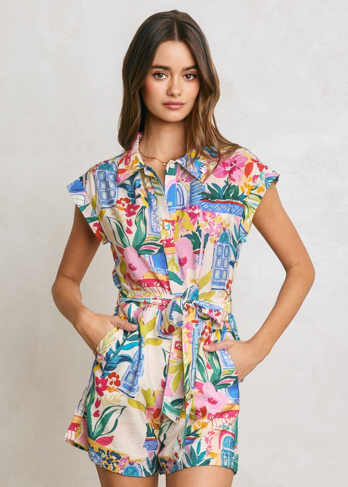 Colorful button-down romper with floral and architectural print, short sleeves, and waist tie belt.