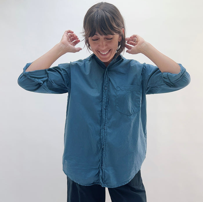 Model wearing the Alix Top in Moonlit Ocean, a relaxed teal button-front shirt with a band collar, chest pocket, and rolled sleeves, styled with navy pants