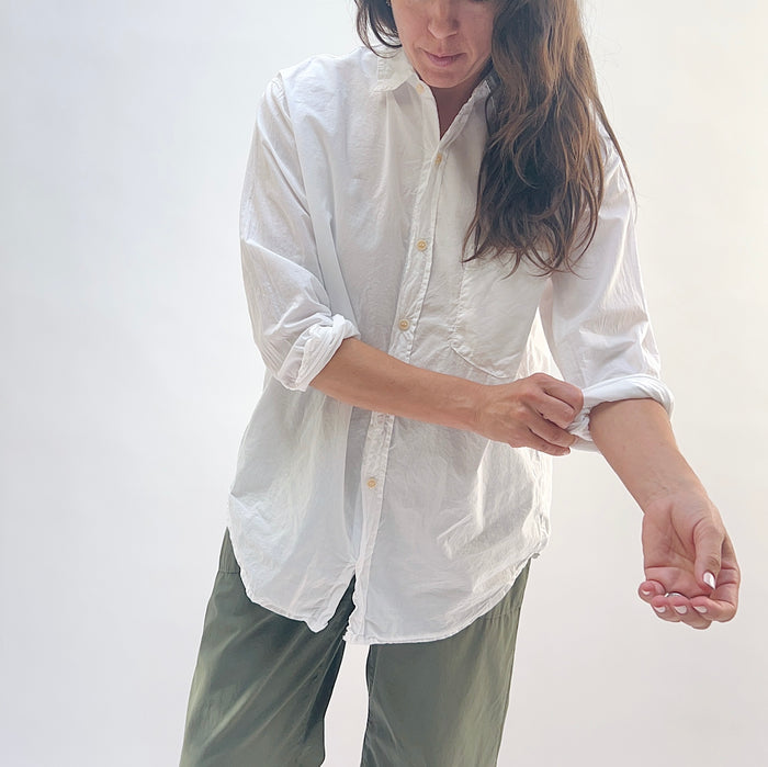 Alix Top in White — three-quarter front view, model rolling up sleeve to show cuff detail and gold buttons