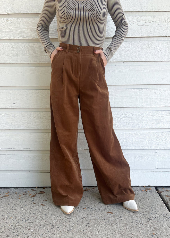Brown corduroy pants with high waist, pleated front, and wide leg silhouette on model wearing gray ribbed sweater.