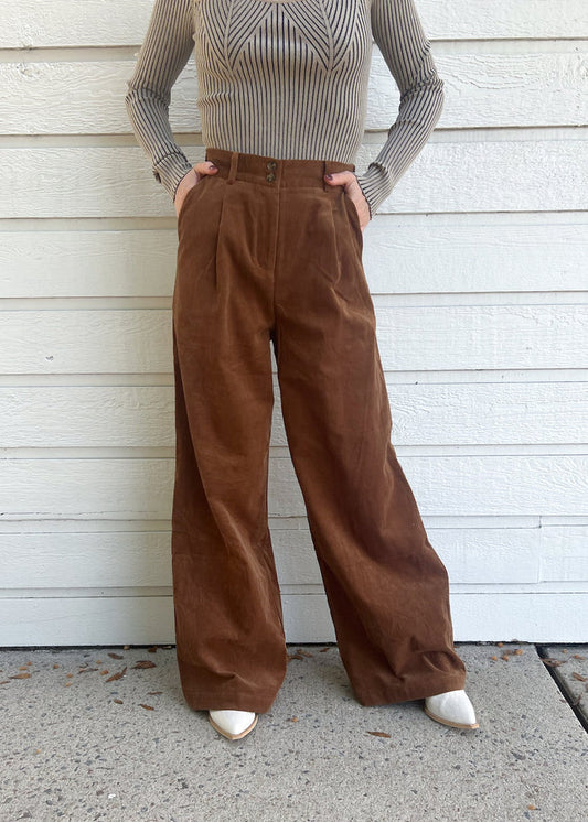 Brown corduroy pants with high waist, pleated front, and wide leg silhouette on model wearing gray ribbed sweater.