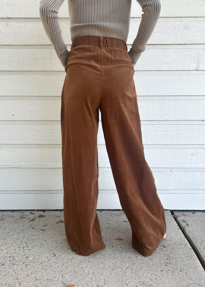 Brown corduroy pants with elastic waistband, shown from back view on model wearing gray ribbed sweater.