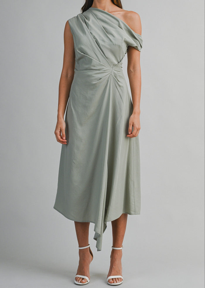 Sage green one-shoulder midi dress with draped fabric and twisted waist detail on model wearing white sandals.