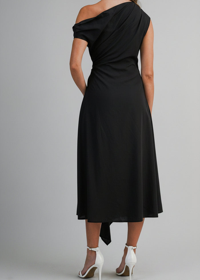 Black one-shoulder midi dress with draped neckline and asymmetrical hem on model wearing white heels.