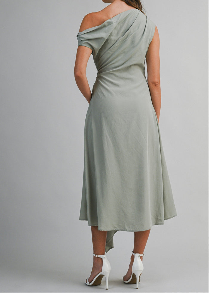 Sage green one-shoulder midi dress with draped neckline and asymmetrical hem, worn with white strappy heels.