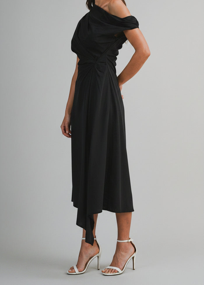 Black one-shoulder midi dress with draped neckline and asymmetrical hemline on model wearing white heeled sandals.