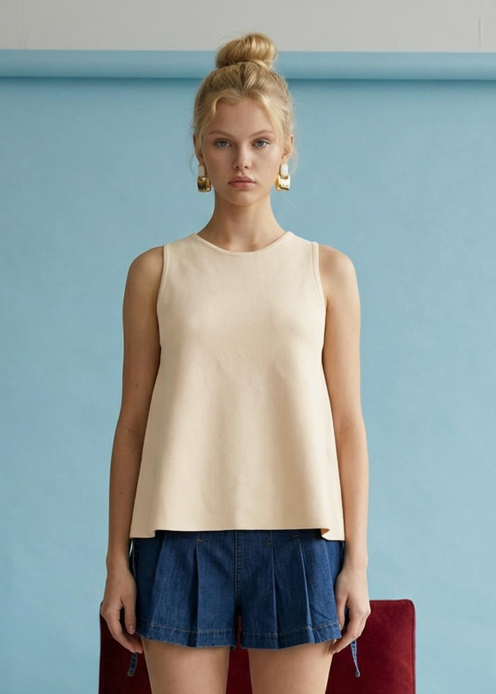 Cream sleeveless linen top with round neckline worn with dark denim shorts.