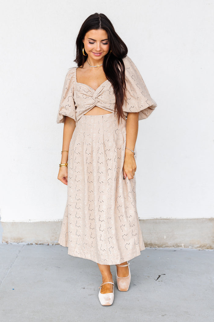 Beige eyelet midi dress with twisted front cutout and puffed sleeves worn with white platform shoes.