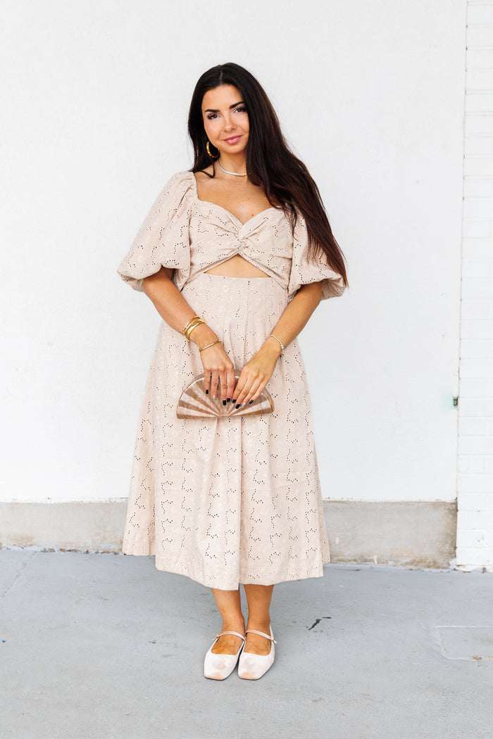 Beige midi dress with eyelet pattern, puffed sleeves, and twisted cutout at waist.
