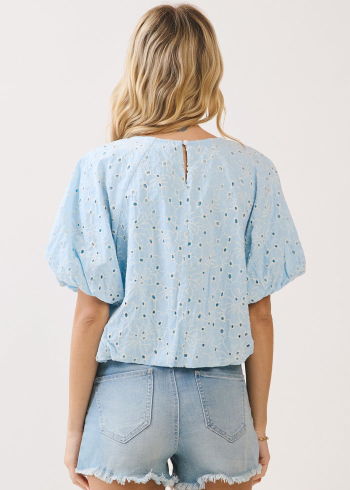 Light blue eyelet top with puffed bubble sleeves and button back closure, worn with light wash denim shorts.